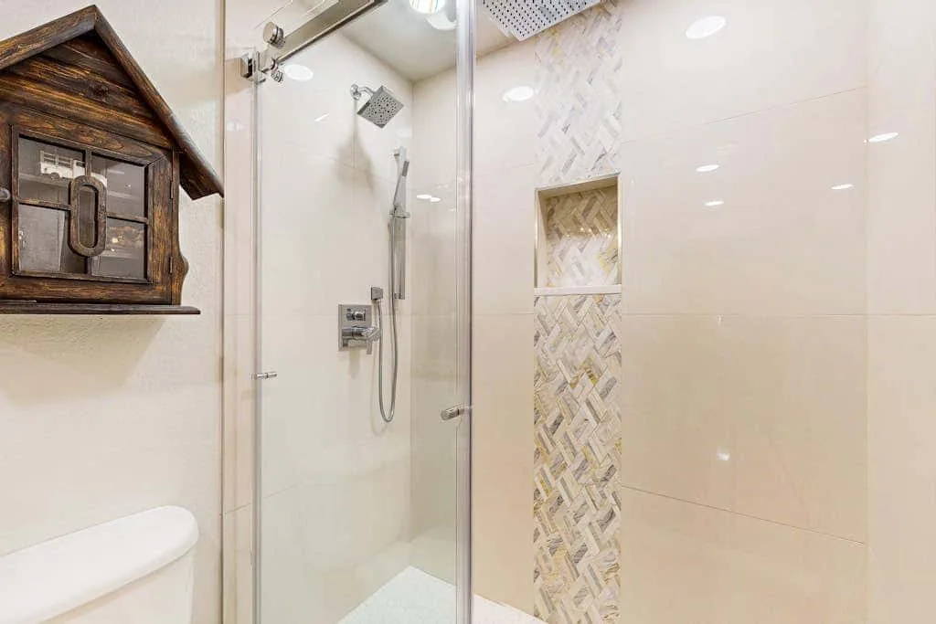 A bright tiled bathroom with a glass shower and wall-mounted wooden decoration.