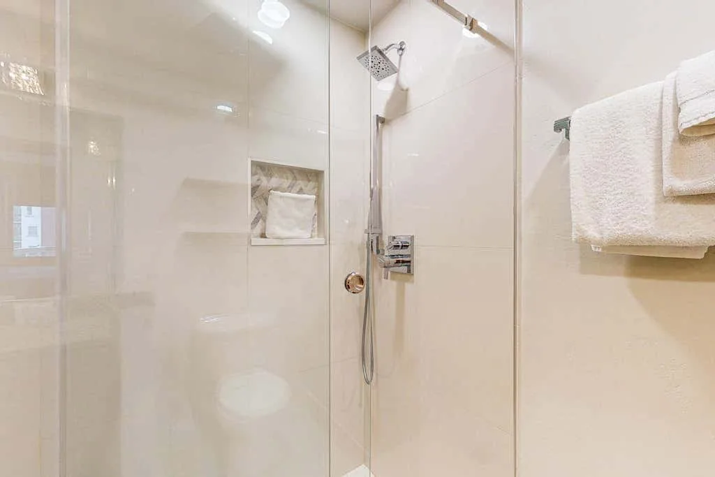 A bright bathroom shower with a handheld showerhead and folded towels.