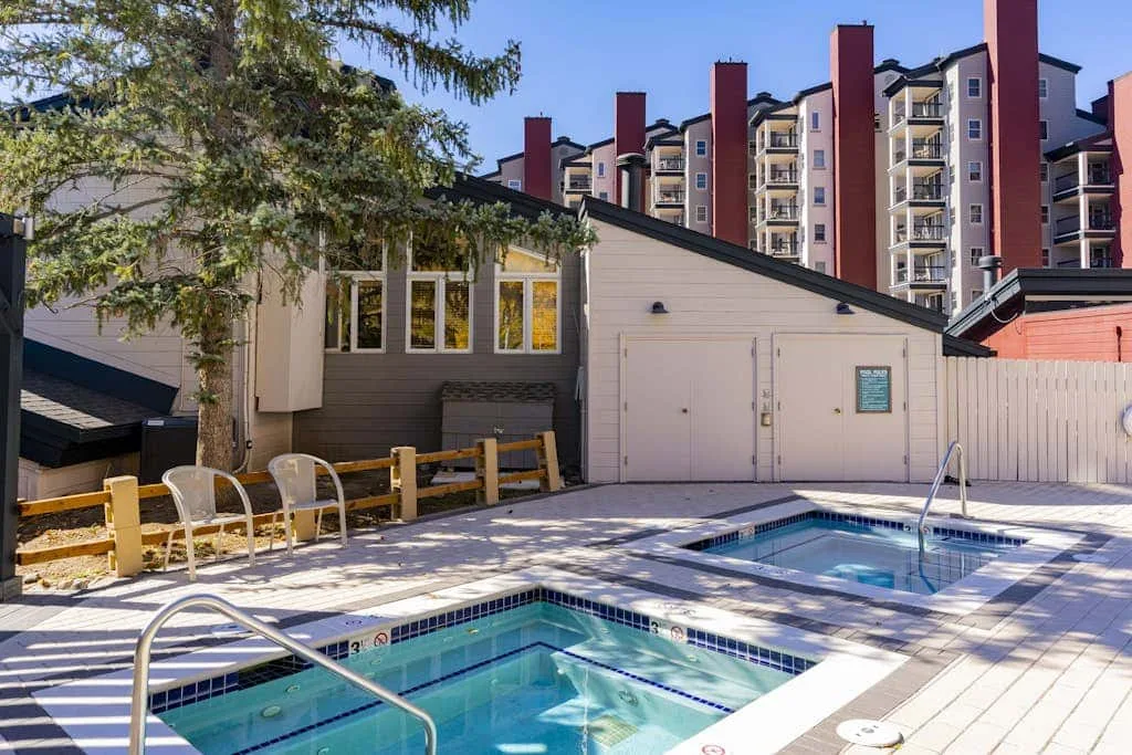 An outdoor swimming pool beside a low building and tall apartment buildings.