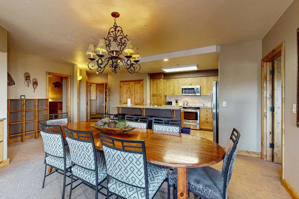 A dining area with a long table and an open kitchen in the background.
