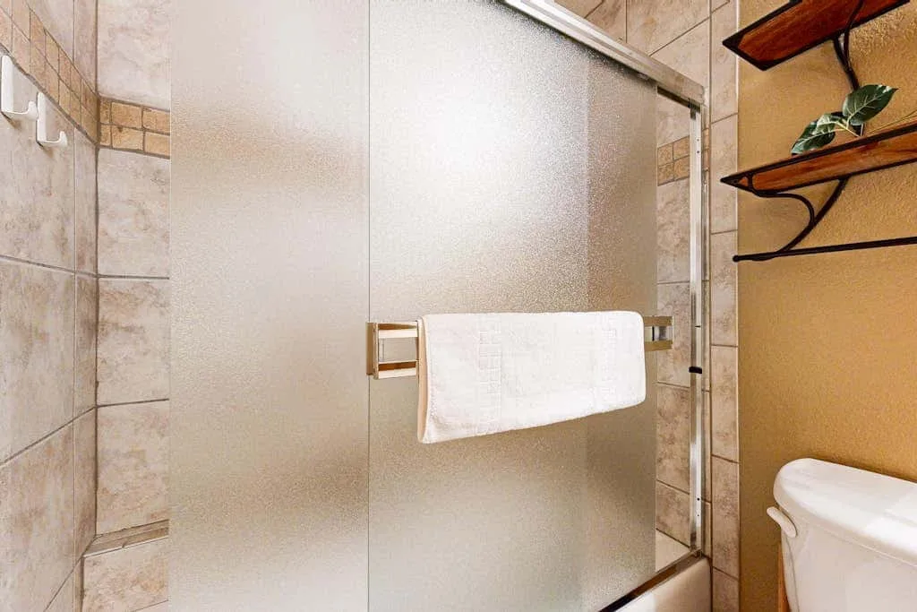 A tiled bathroom with a frosted glass shower and a towel hanging on the door.