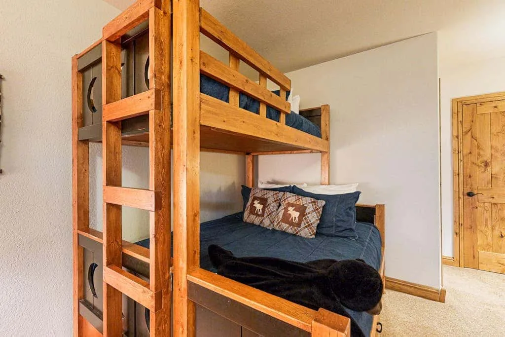 A bedroom with a wooden bunk bed and dark bedding.