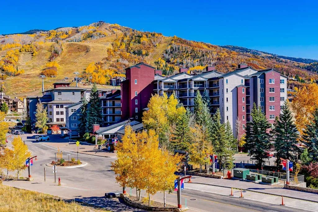 A mountain resort complex stands among colorful autumn trees beneath a clear blue sky.