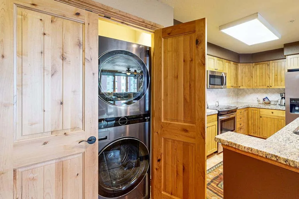 Laundry area with a stacked washer and dryer beside a kitchen.