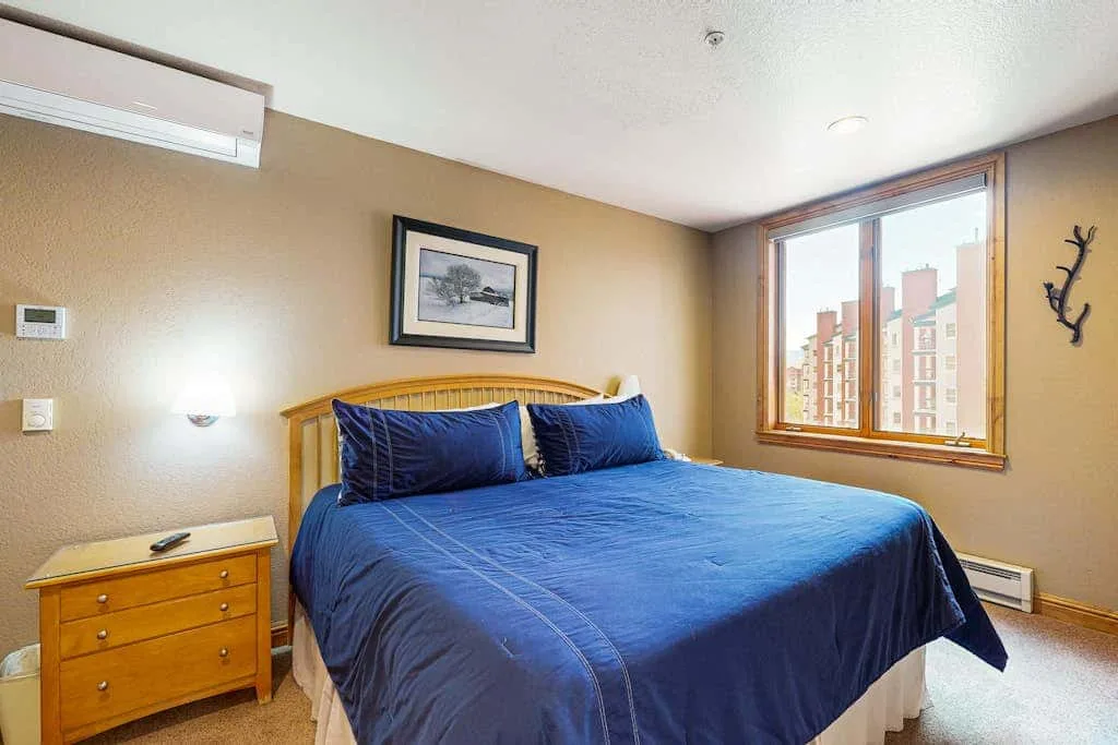 A bedroom with a bed covered in blue bedding beside a large window.