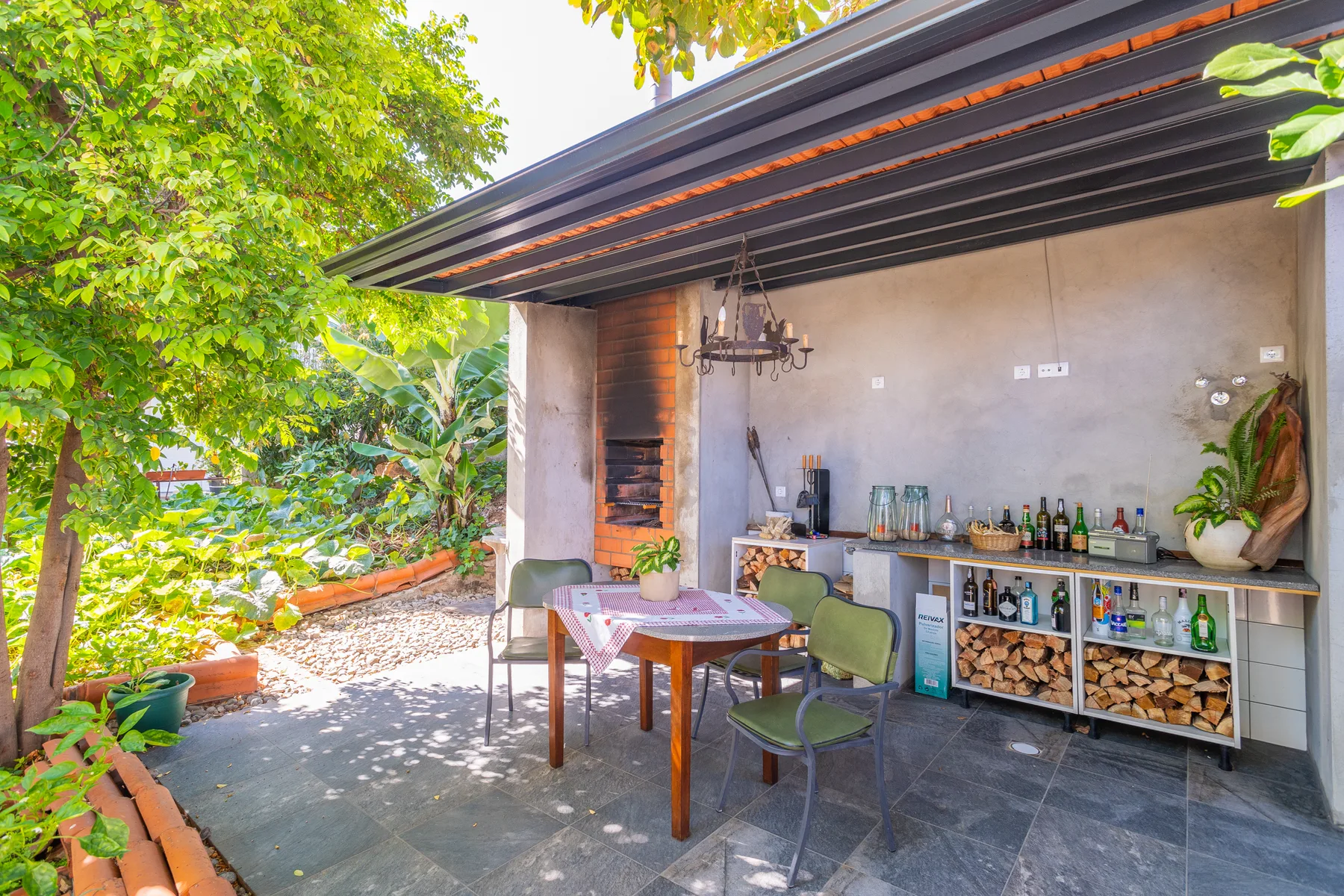Una zona exterior cubierta para comer y tomar algo da a un jardín frondoso.