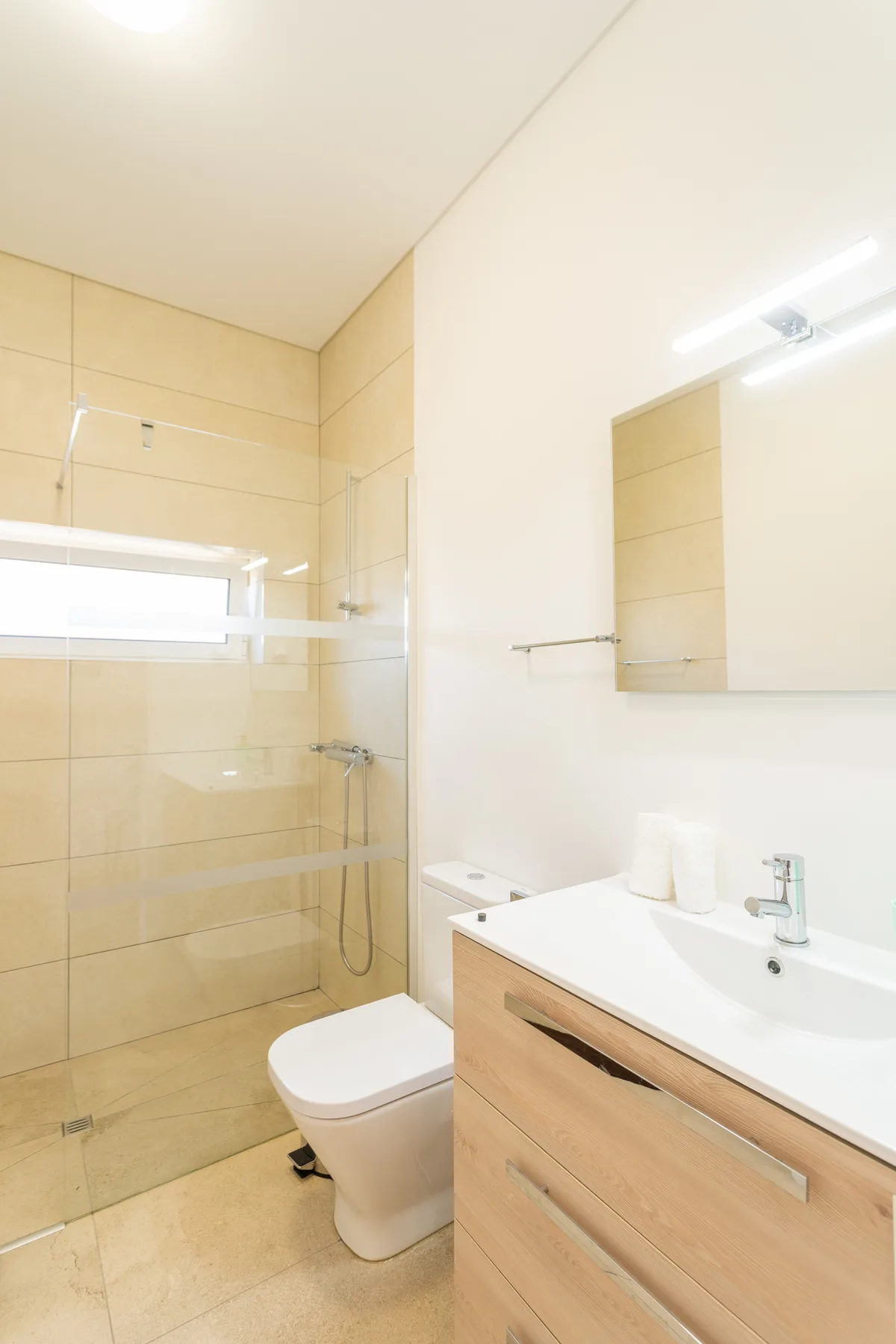 Un baño luminoso con ducha de cristal, inodoro y lavabo.