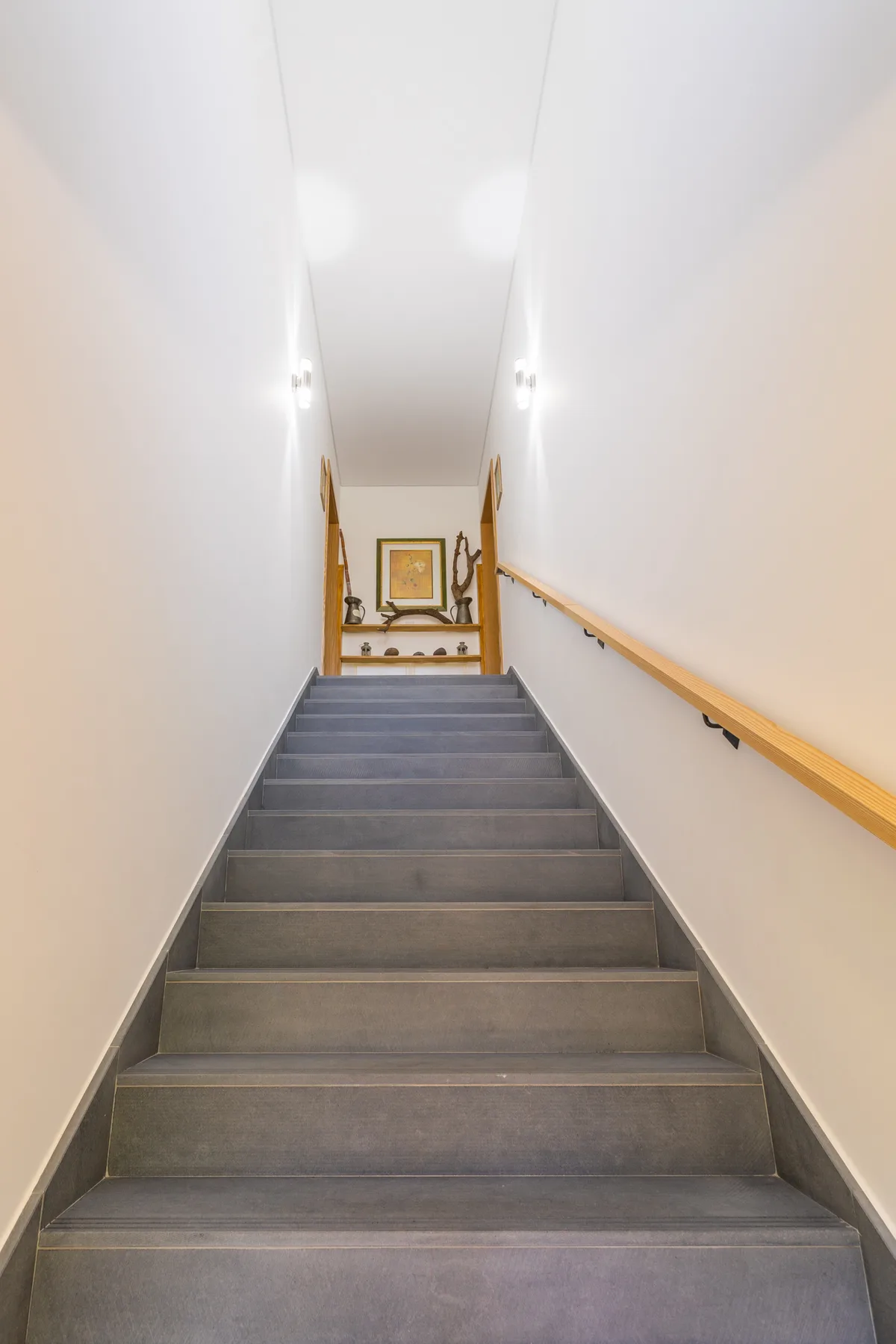 Una escalera con peldaños grises y un pasamanos de madera conduce a un cuadro.