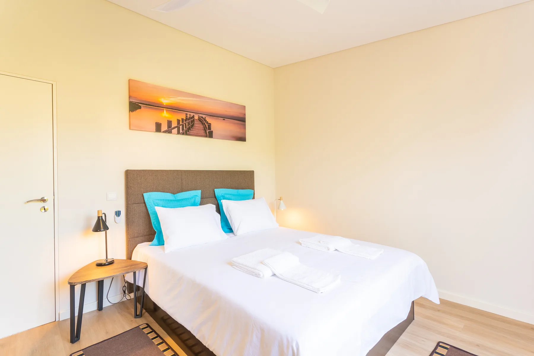 Dormitorio luminoso con ropa de cama blanca y un cuadro sobre la cama.