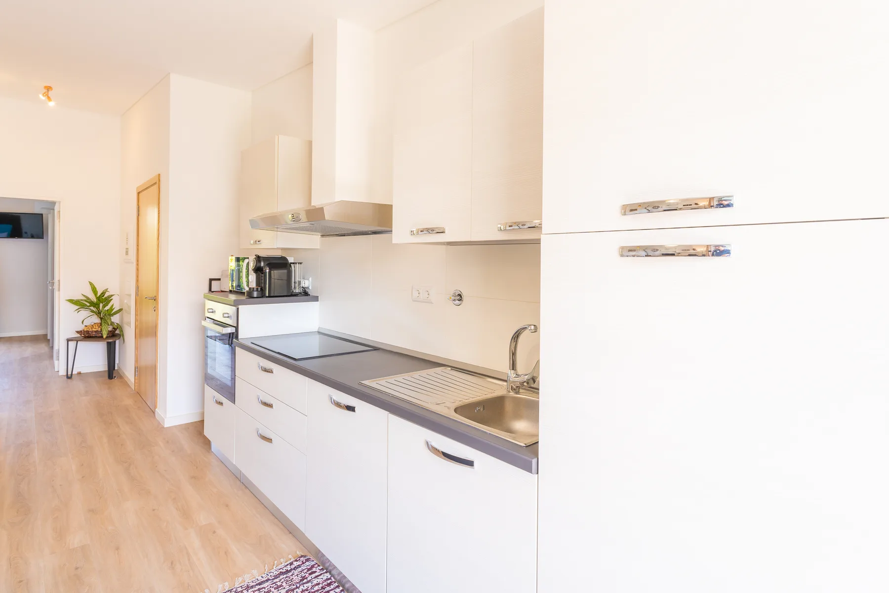 Una cocina luminosa con armarios blancos, una placa de cocina y un fregadero.