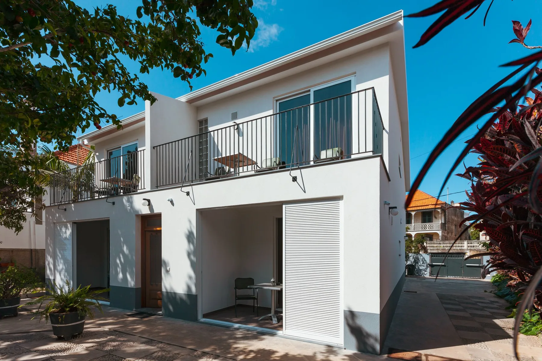 Un edificio de apartamentos blanco y moderno con balcones y un patio pavimentado.