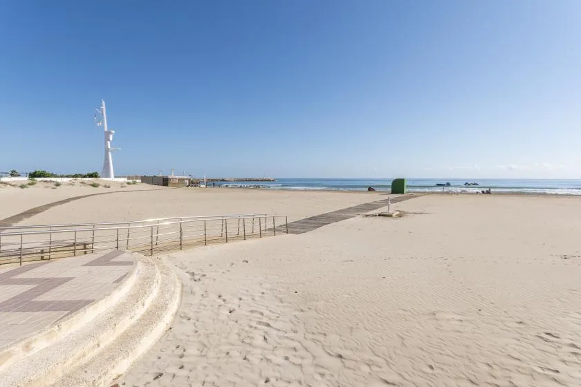 A sandy beach and paved promenade extend toward the calm sea under a clear sky.