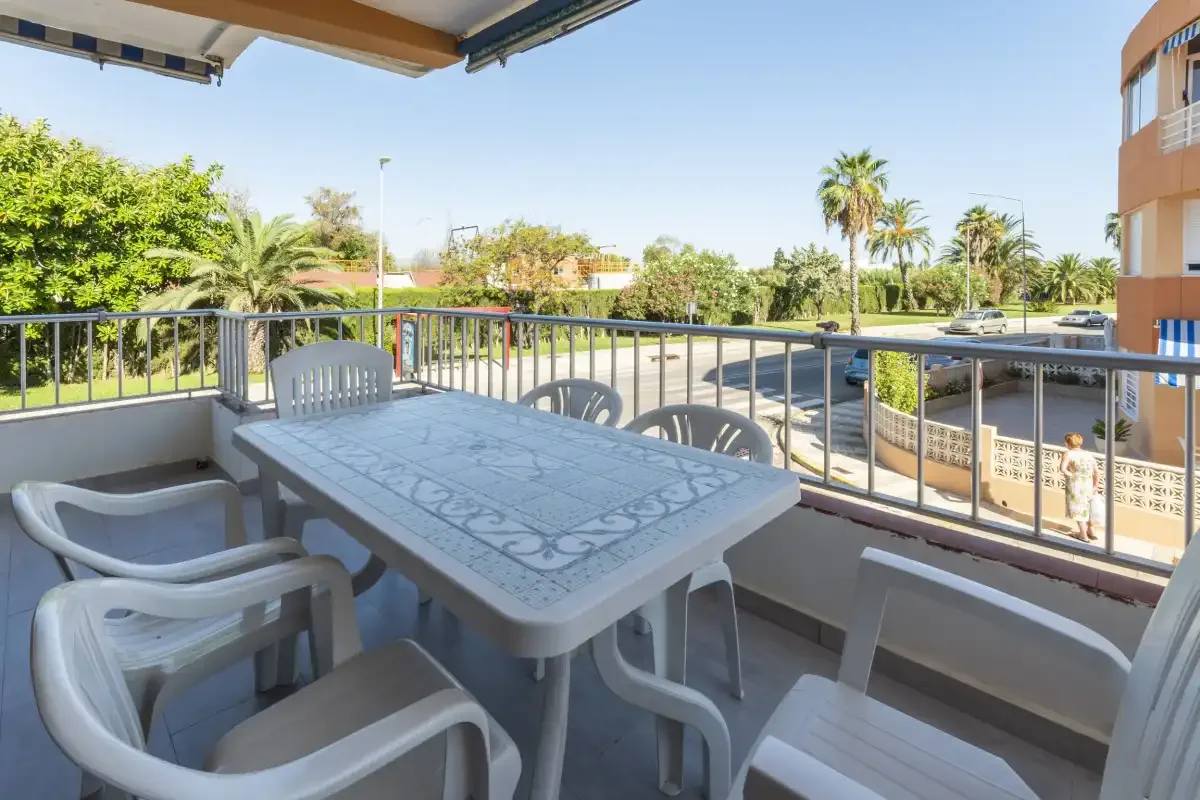 A covered terrace with a table and seating overlooks a tree-lined street.