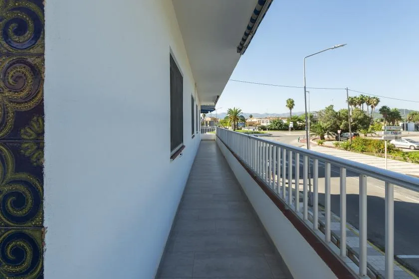 A narrow outdoor balcony runs beside a white building, overlooking a street.