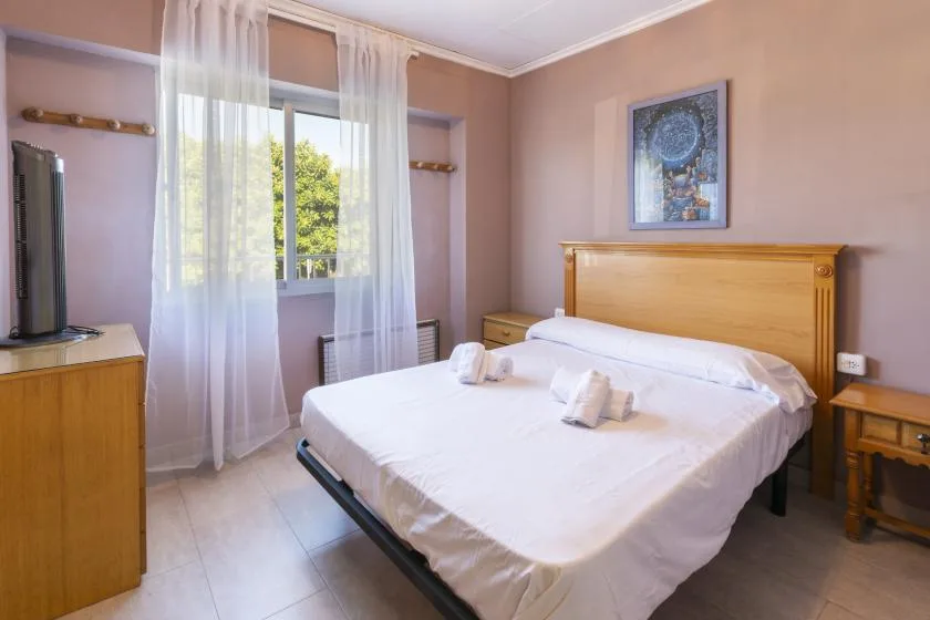 A bedroom with a neatly made bed and sheer curtains over the window.