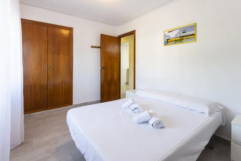 A bright bedroom with a neatly made bed and wooden wardrobes.
