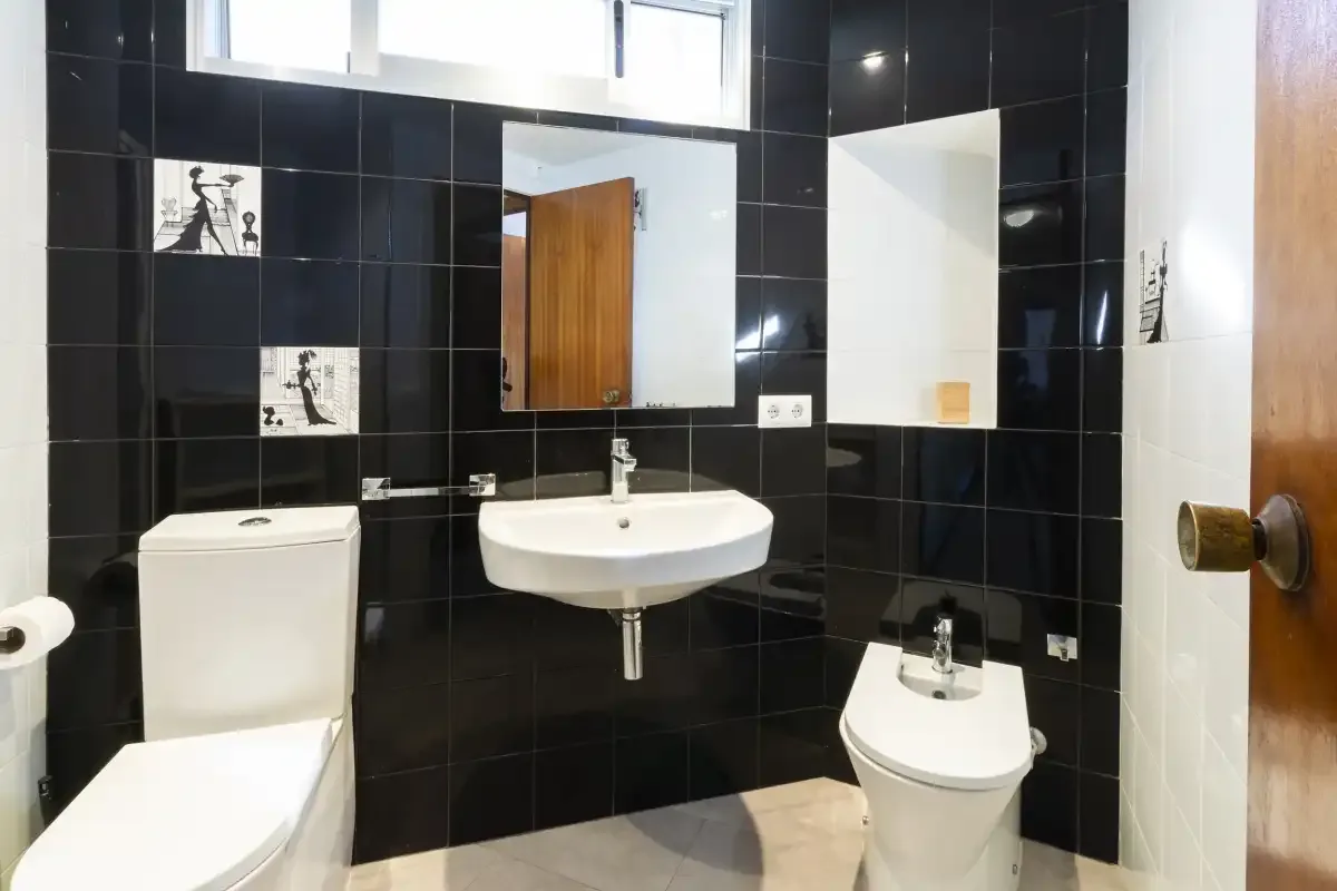A bathroom with a sink, toilet, and black tiled walls.