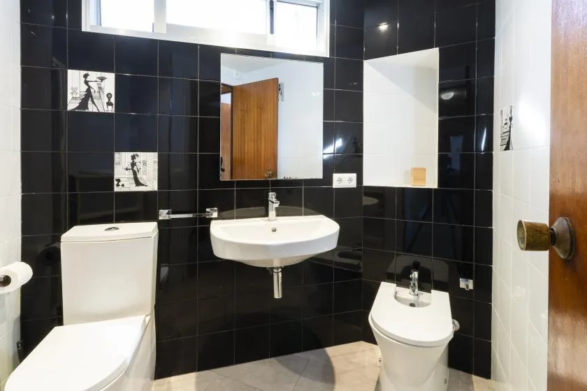 A tiled bathroom with a sink, toilet, and mirror.
