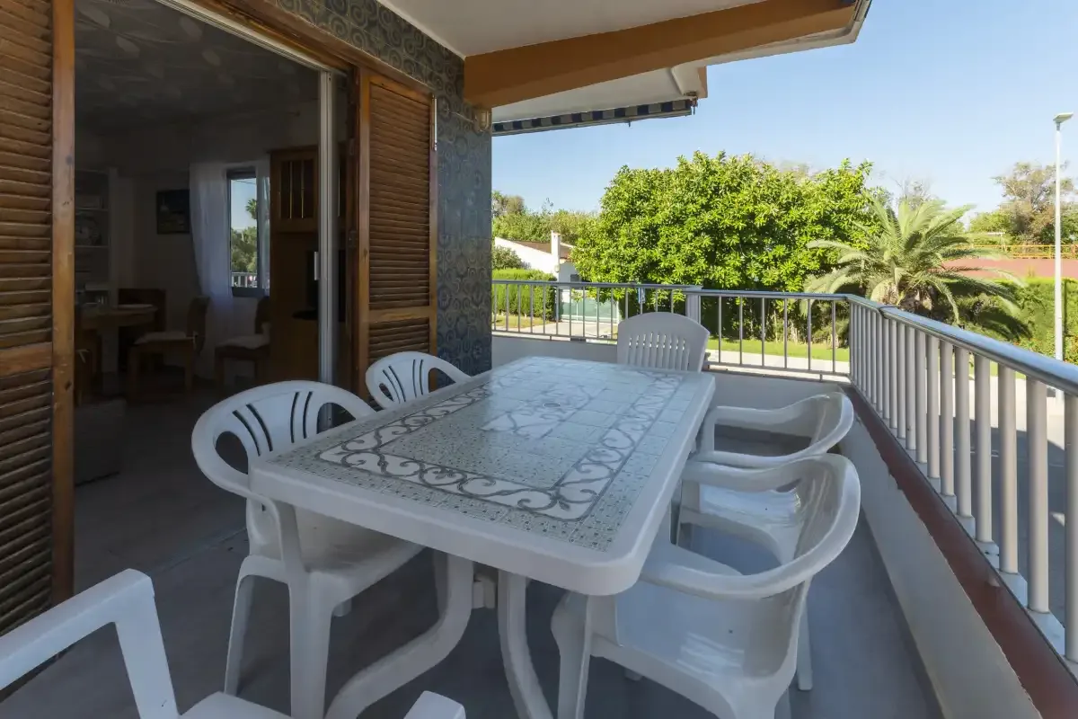 A covered terrace has a white outdoor table and seating beside a railing.
