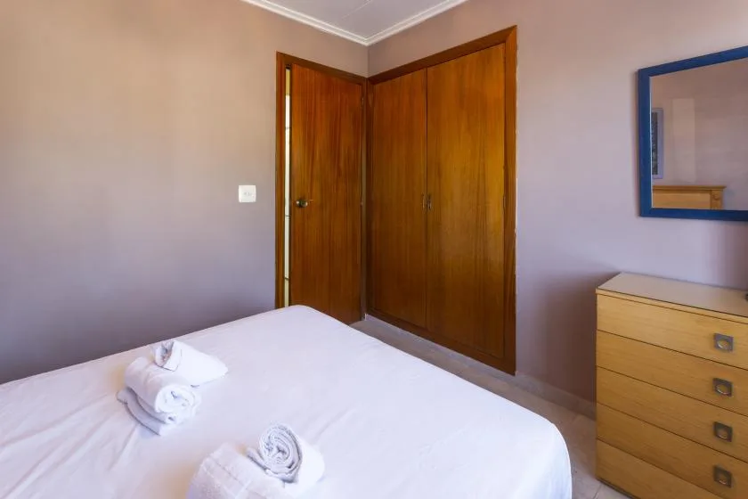 A bedroom with a neatly made bed, wooden wardrobe, and dresser.