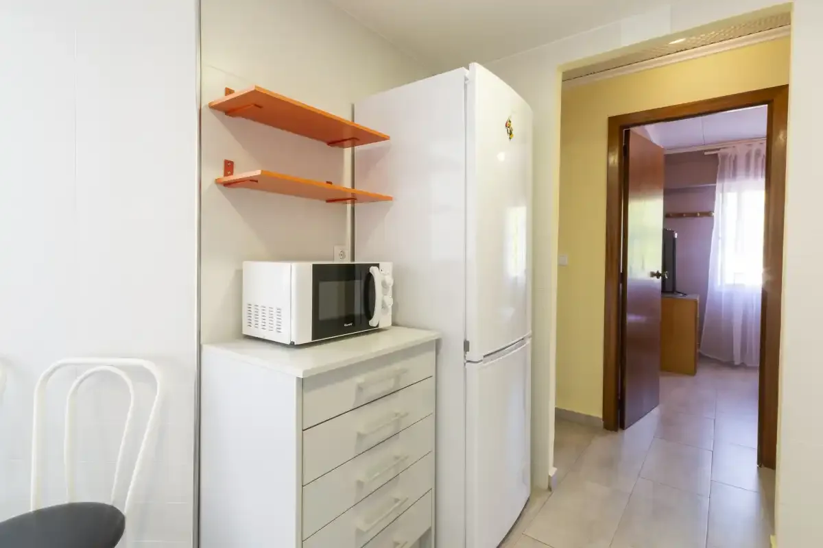A compact kitchen area with a microwave, refrigerator, and open shelves.