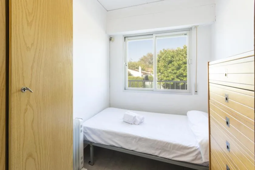 A bright bedroom with a single bed beneath a large window.