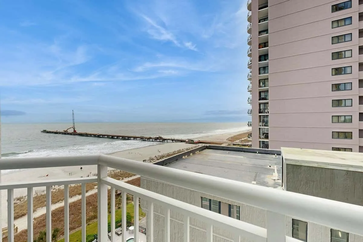 A balcony overlooks the sea and a long pier beside a high-rise building.