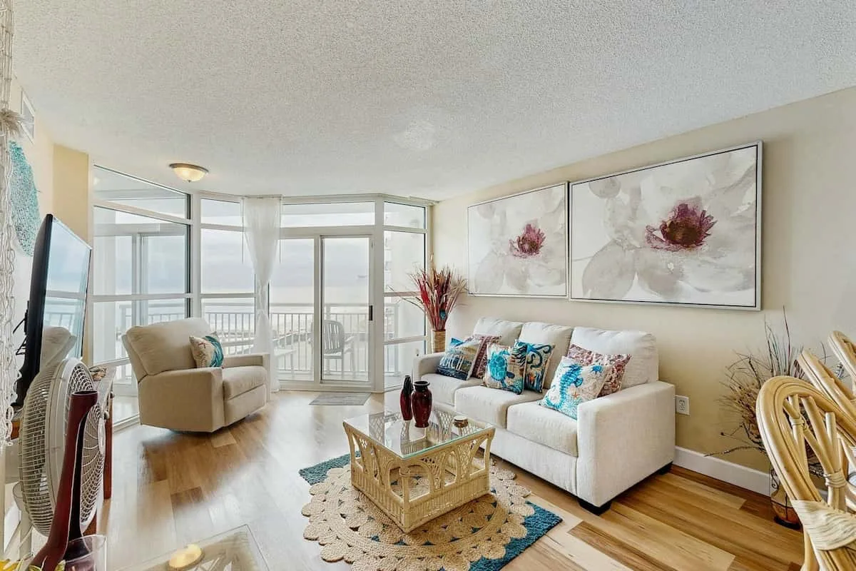 A bright living room with seating, large windows, and floral wall art.