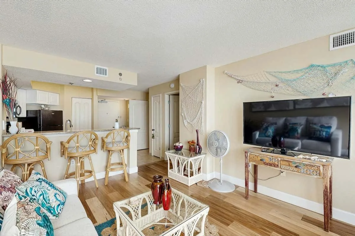 Living room with a television, seating, and an adjoining kitchen.
