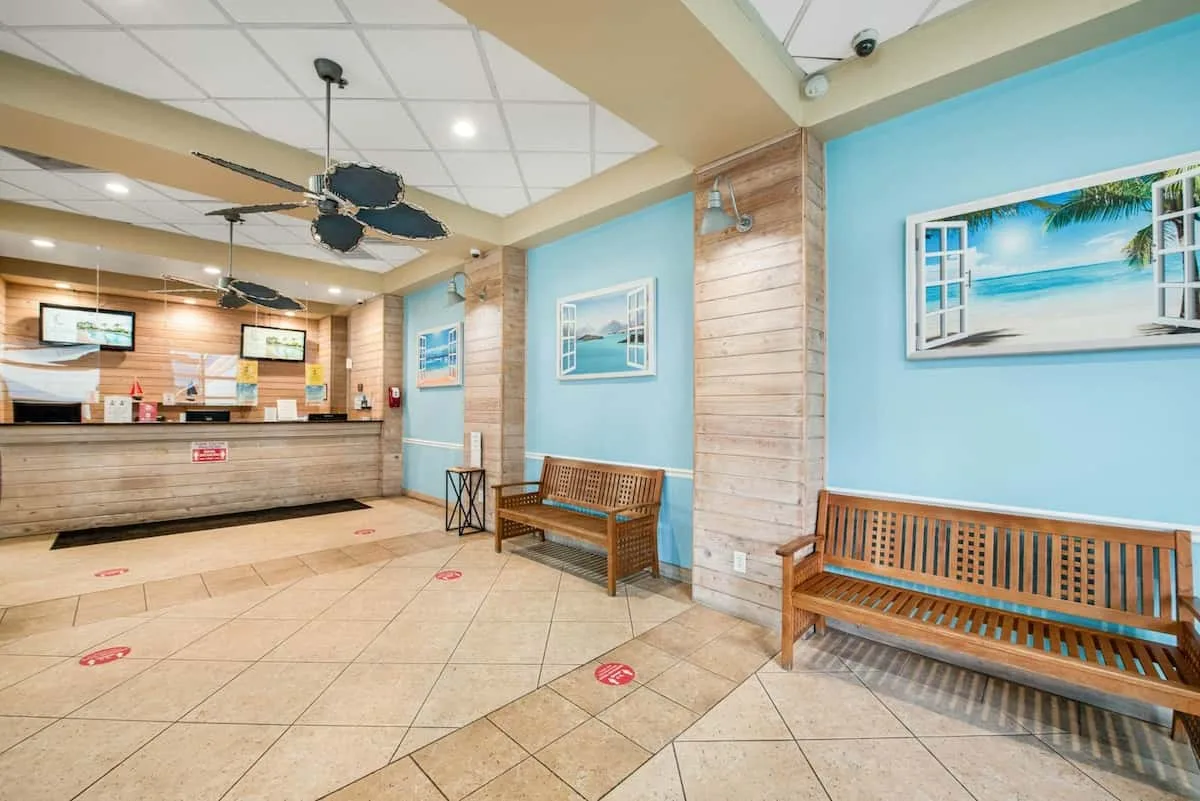 A reception lobby with a front desk, wooden benches, and framed beach scenes.