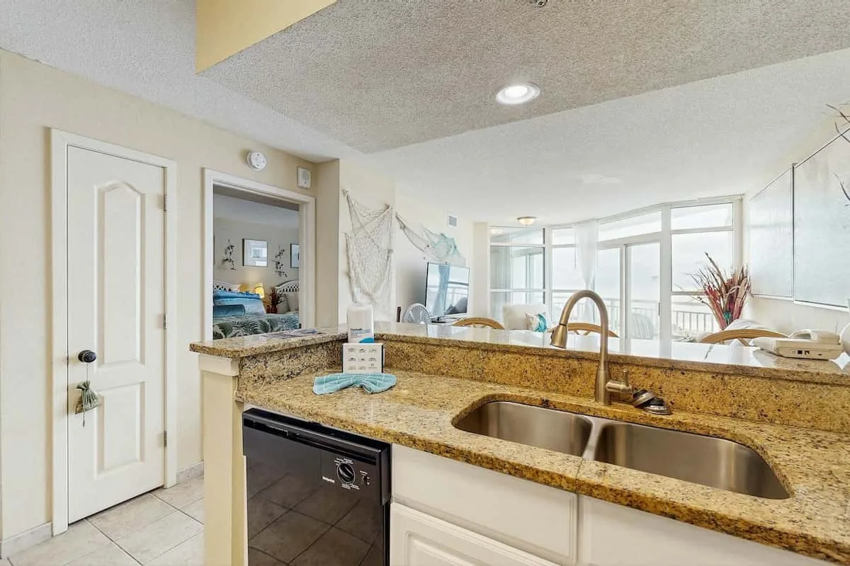 A bright kitchen with a granite countertop, sink, and large windows.