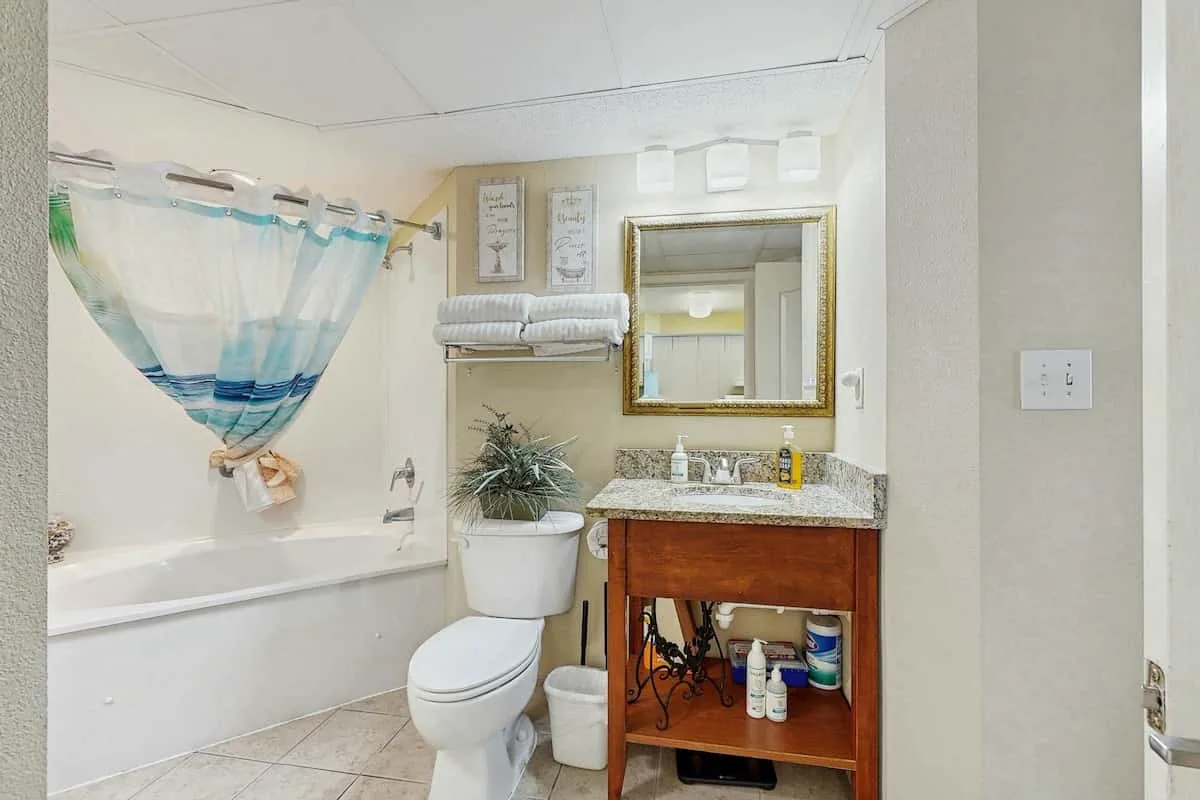 A bathroom with a bathtub, toilet, and wooden vanity beneath a mirror.