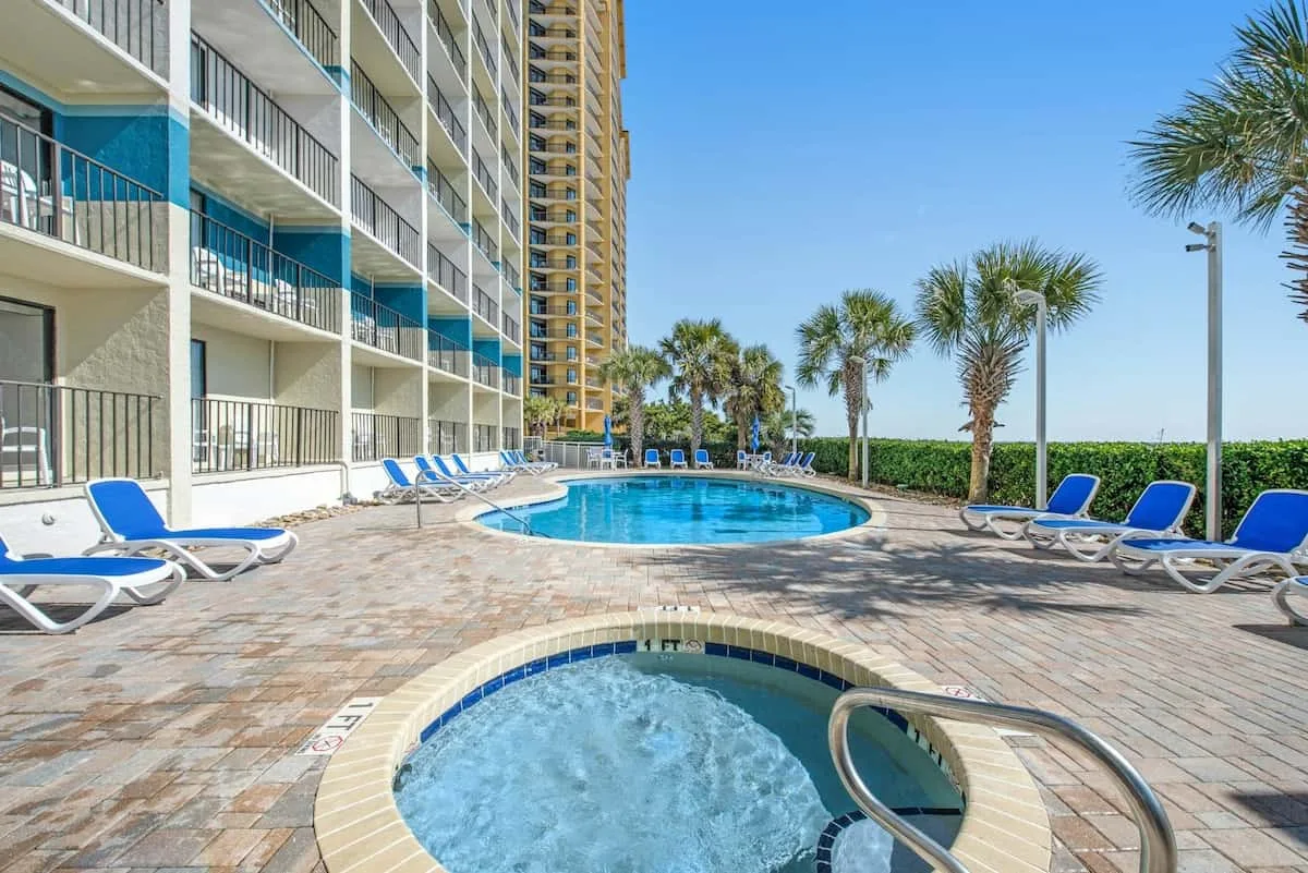 An outdoor pool and spa sit beside a high-rise building under a clear sky.