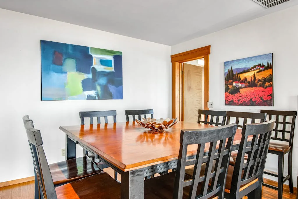 A dining room with a wooden table, chairs, and colorful wall art.