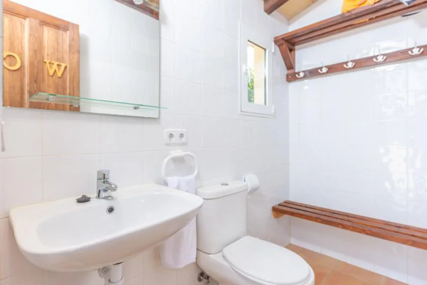 A tiled bathroom with a sink, toilet, and wooden wall shelving.