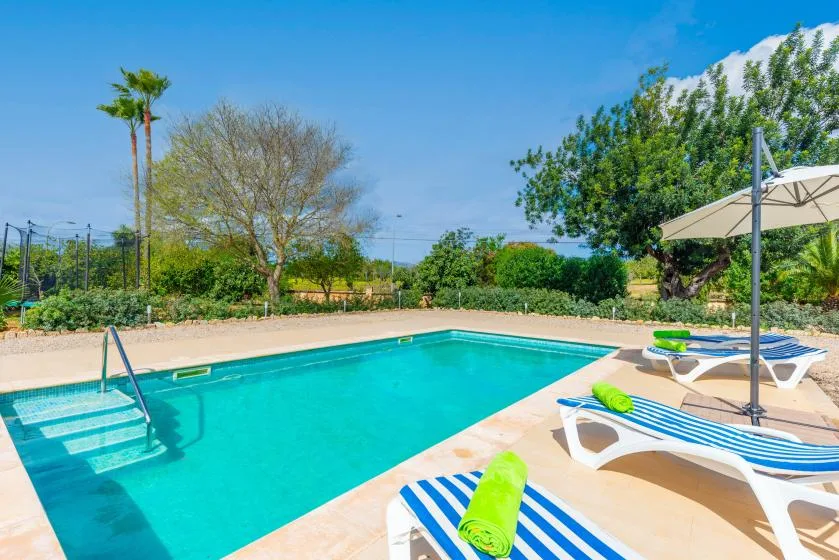 An outdoor swimming pool with striped loungers and a large shade umbrella.