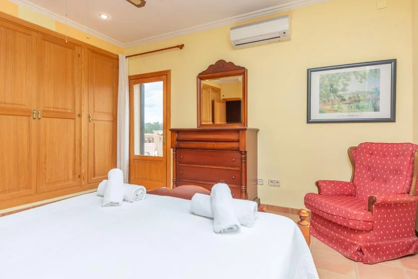 A bedroom with a bed, wooden storage cabinets, and a red upholstered chair.