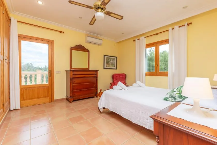 A bedroom with a bed, wooden dresser, and windows overlooking greenery.