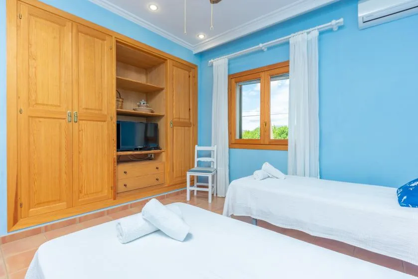 A bright bedroom with wooden wardrobes, two beds, and a window.