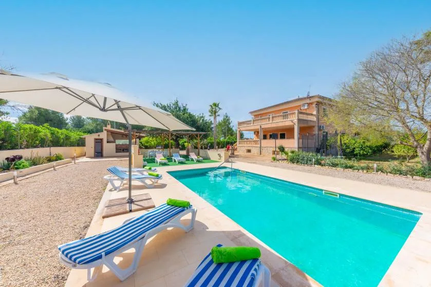 An outdoor swimming pool sits beside a house and shaded lounge seating.