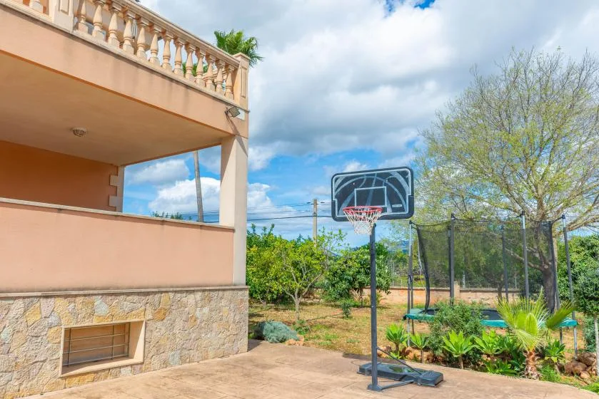 A basketball hoop stands beside a fenced outdoor court near a building.