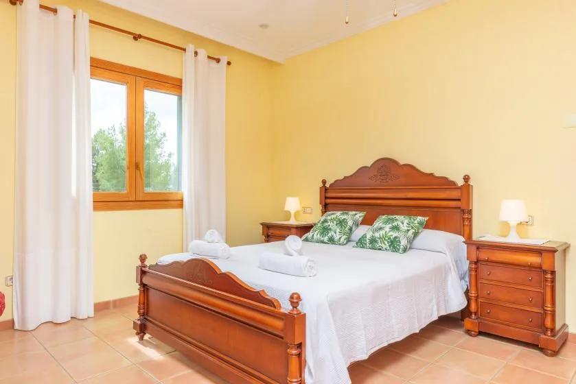 A bedroom with a wooden bed, white bedding, and a window with curtains.