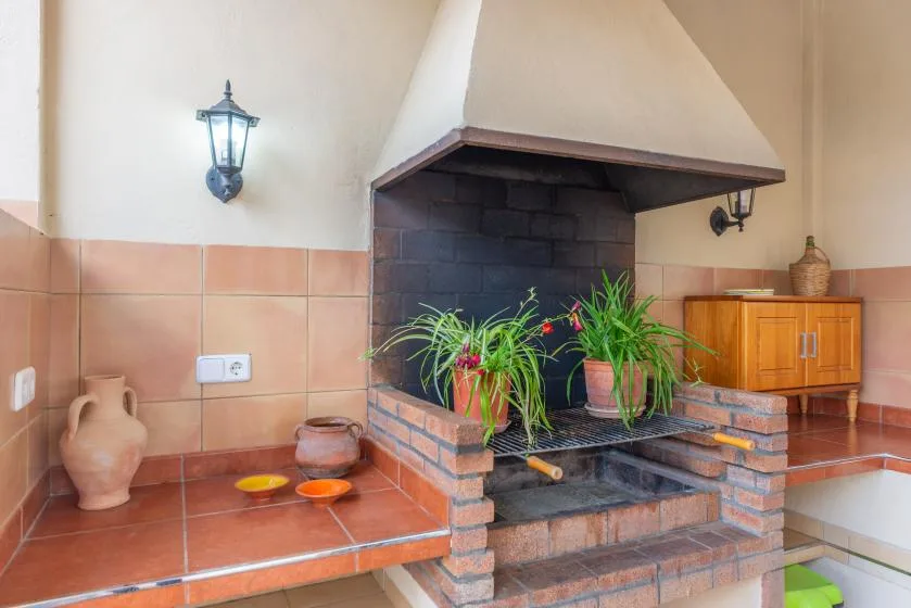 A brick barbecue hearth with potted plants sits in a tiled indoor cooking area.