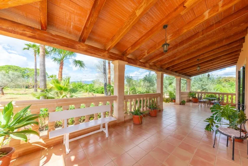 A covered patio with tiled flooring, a bench, and views of the garden.