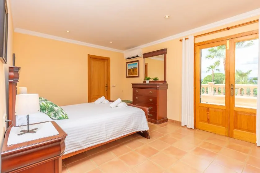 A bedroom with a bed, a wooden dresser, and glass doors opening onto a balcony.