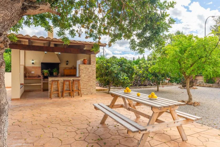 An outdoor dining area with a wooden picnic table beside an open-air kitchen.