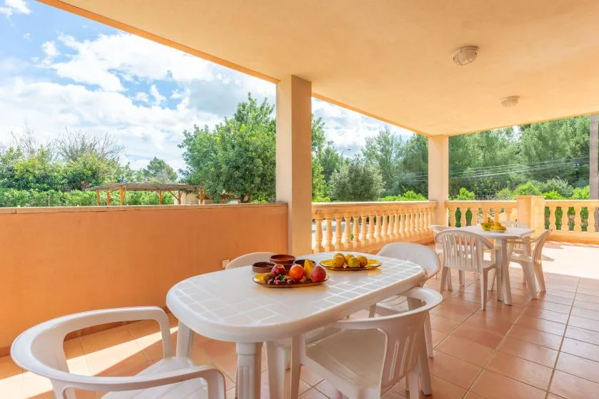 A covered terrace has seating around a table with fruit and other food.