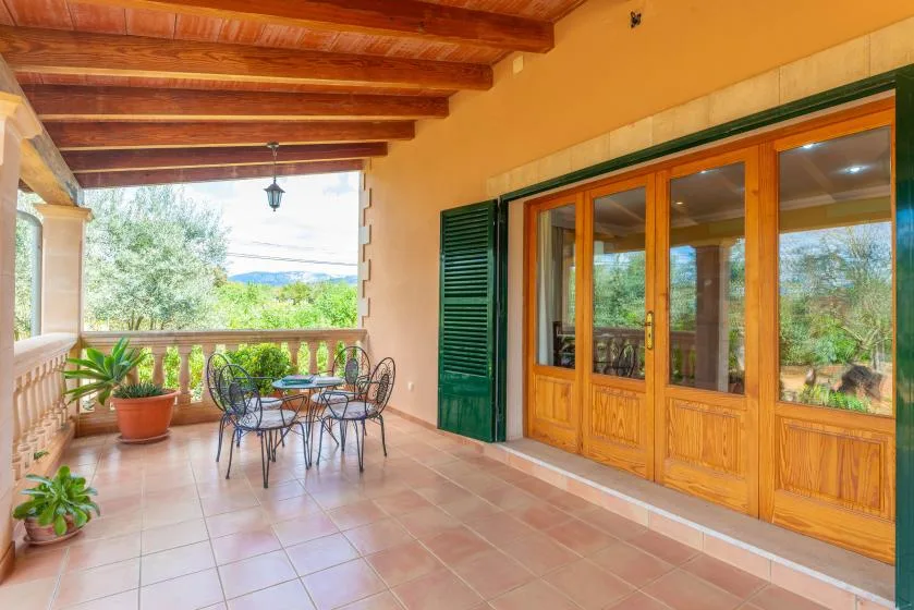 A covered patio with a table and chairs beside wooden-framed glass doors.