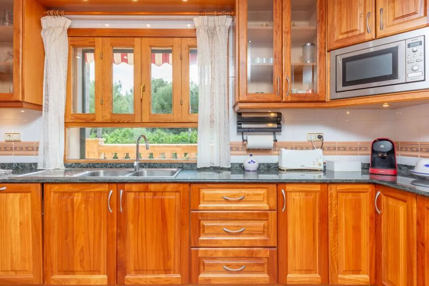 A wood-cabinet kitchen with a sink beneath a curtained window.