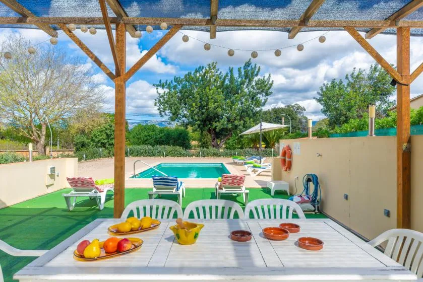 A covered outdoor dining area overlooks a swimming pool and landscaped garden.